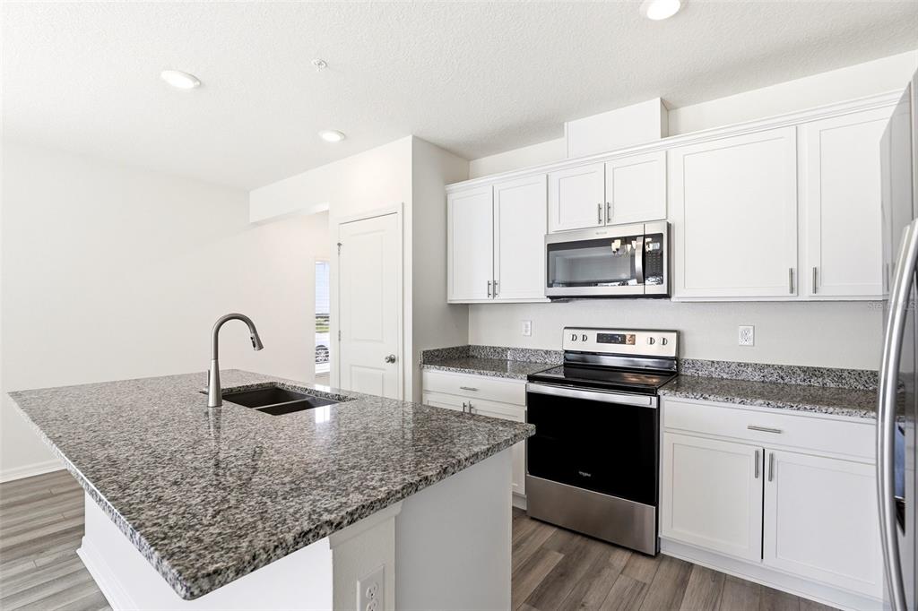 A kitchen features white cabinets, granite countertops, a center island, and stainless steel appliances — 2274 CARRABELLE WAY, SANFORD, FL