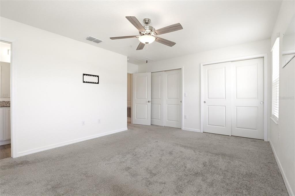 A bedroom with white walls, gray carpeting, a ceiling fan, and two sets of closet doors — 2274 CARRABELLE WAY, SANFORD, FL