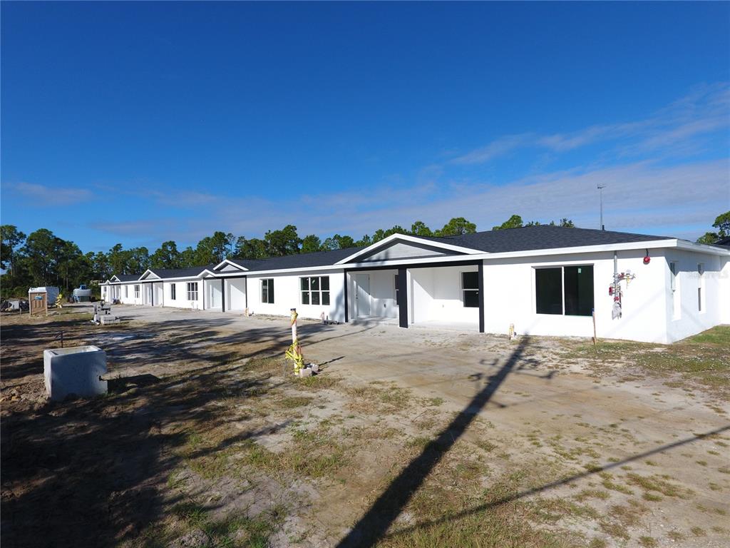 A row of newly constructed white single-story residential units under a clear blue sky — 1215 CAPRICORN BOULEVARD, PUNTA GORDA, FL