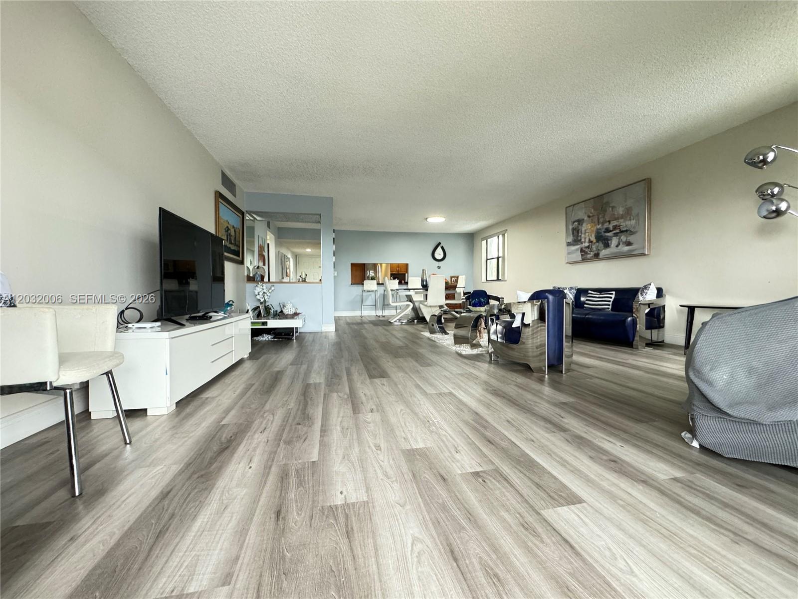 A spacious living and dining area features light wood-look flooring and modern furniture — 16051 Blatt Blvd # 401, Weston FL 33326, WESTON, FL