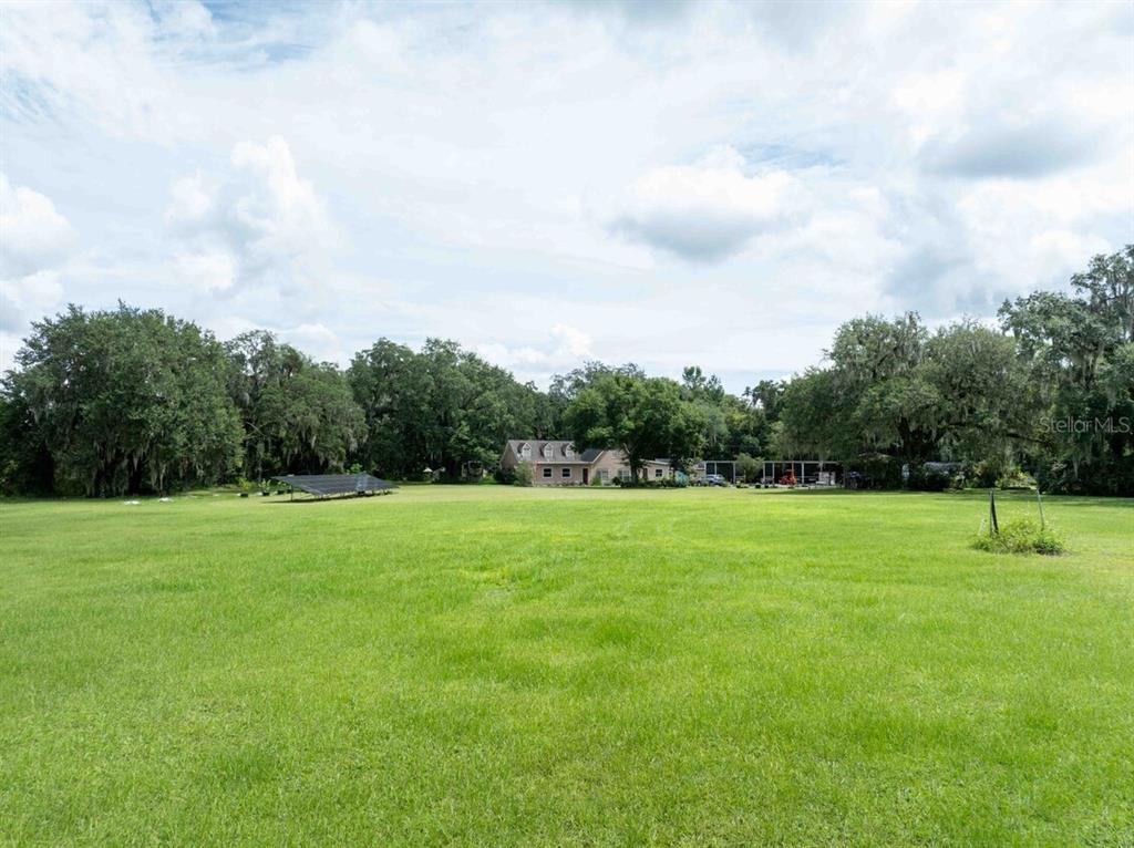 A large, grassy field leads toward a house surrounded by mature trees and solar panels — 3500 N US HIGHWAY 301, WILDWOOD, FL