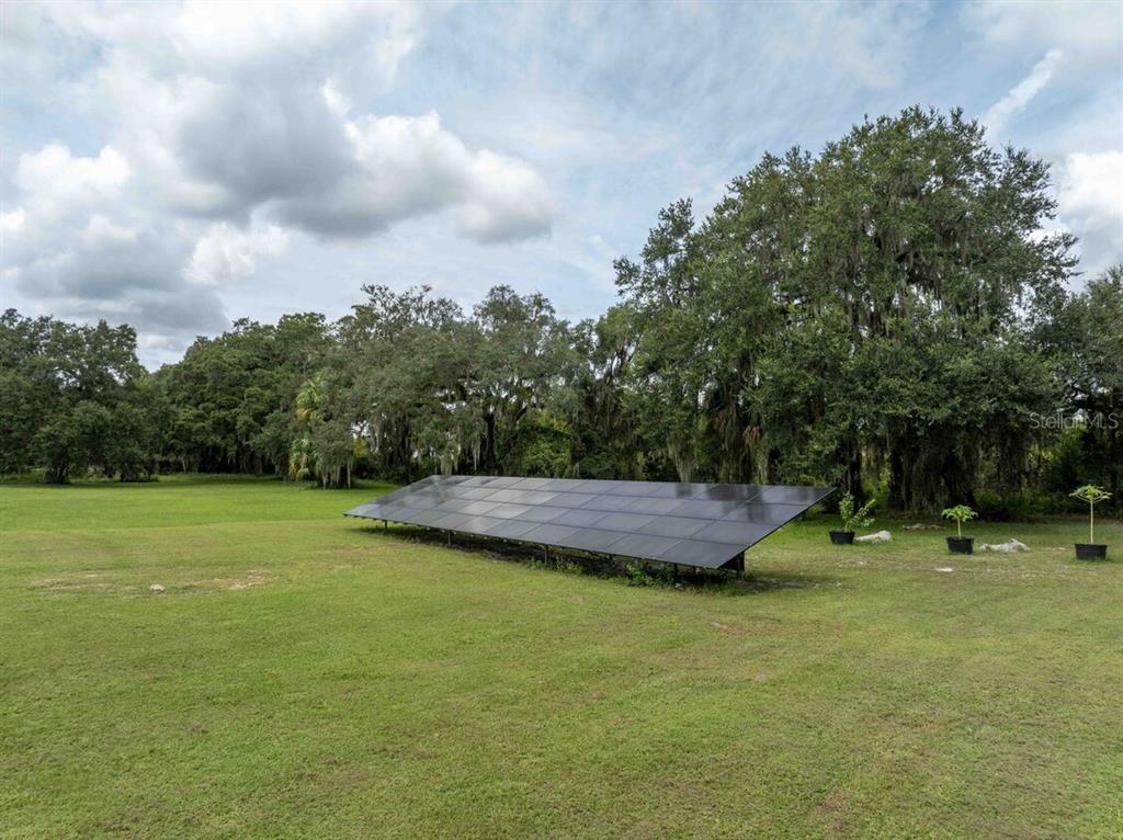 A ground-mounted solar panel array sits in a grassy yard surrounded by mature trees — 3500 N US HIGHWAY 301, WILDWOOD, FL