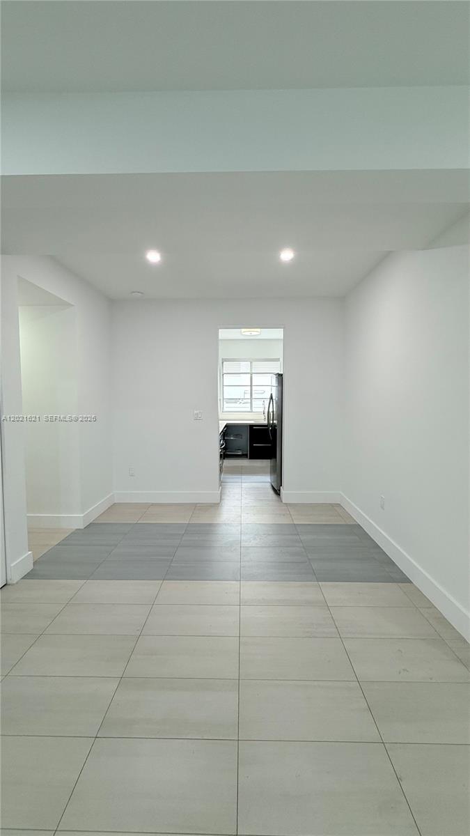 A view of a minimalist dining area with light-colored tile floors leading into a kitchen — 2021 Meridian Ave # 6, Miami Beach FL 33139, MIAMI BEACH, FL