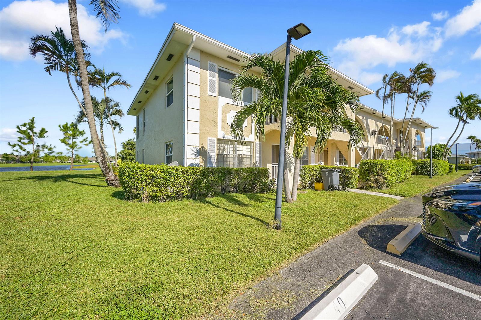 A multi-story apartment building with beige stucco walls stands beside a grassy lawn and parking — 13791 Flora Place # A, Delray Beach FL 33484, DELRAY BEACH, FL