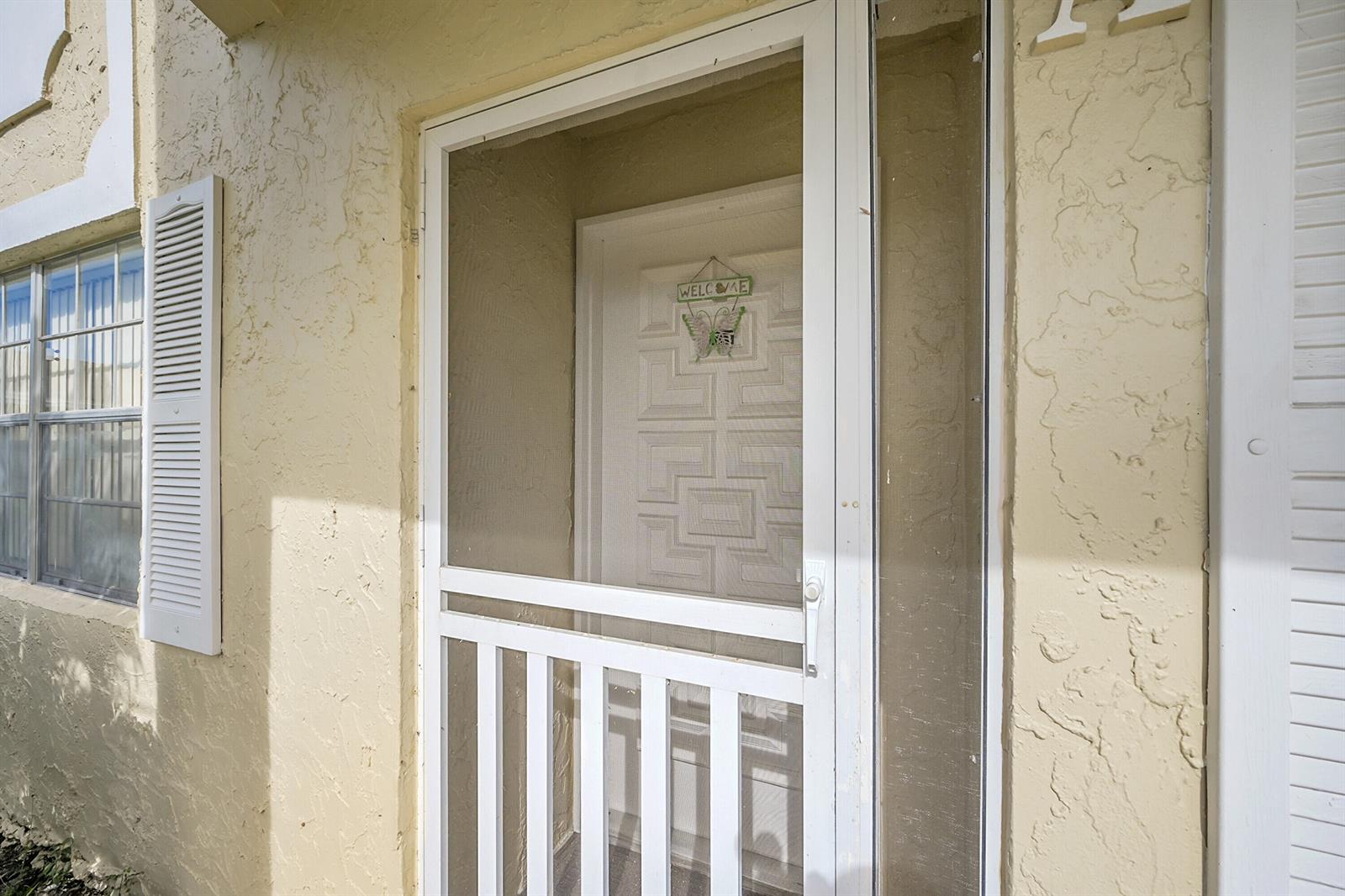 A white screen door leads to a front entrance with a decorative butterfly welcome sign — 13791 Flora Place # A, Delray Beach FL 33484, DELRAY BEACH, FL