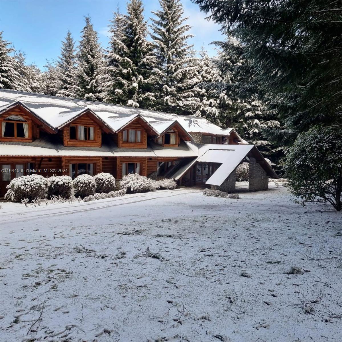 A two-story log cabin with a stone-pillared entryway sits in a snow-covered forest — ARGENTINA Puerto Manzano Villa La Angostura, FL