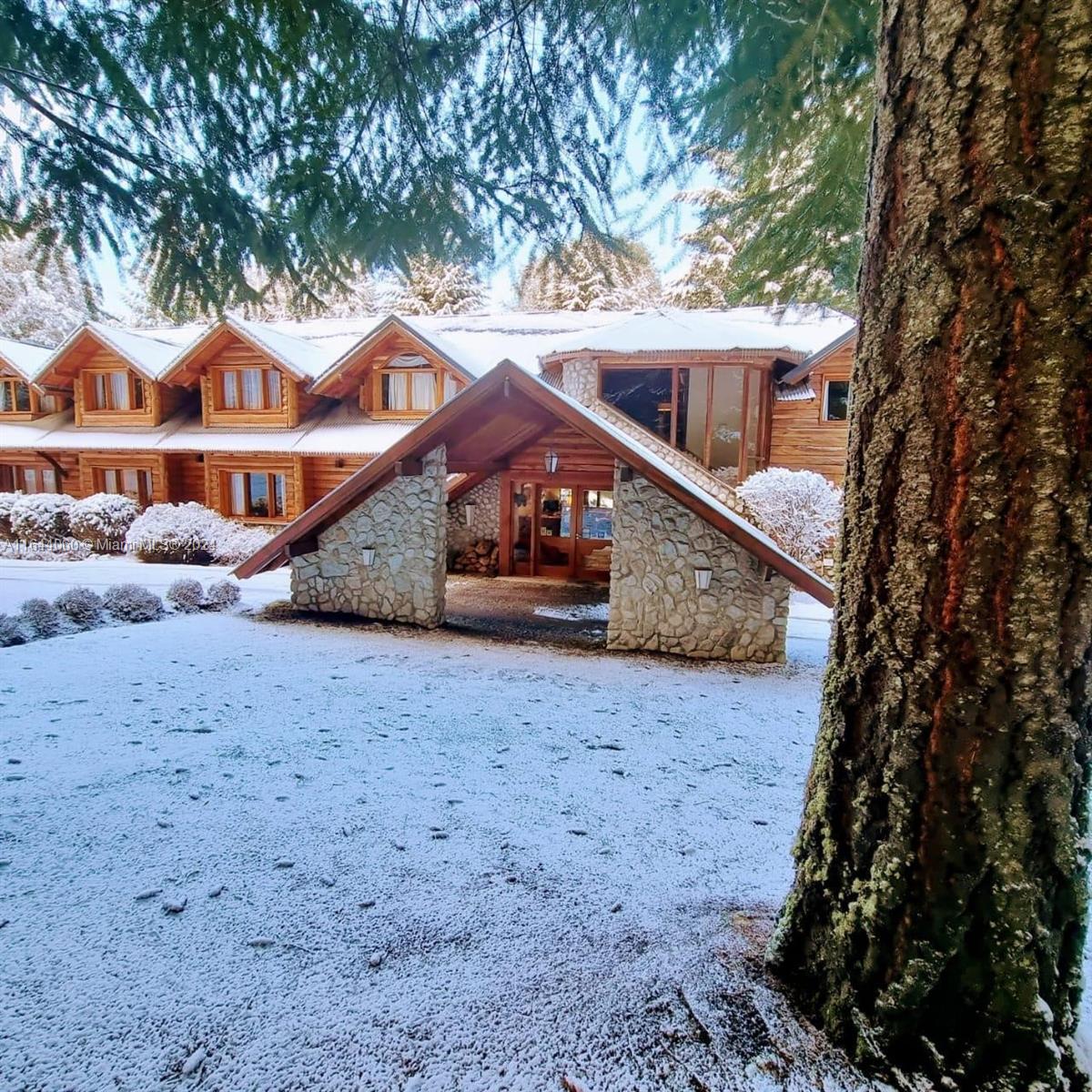 A snow-covered log cabin features a stone-accented entryway and multiple dormer windows — ARGENTINA Puerto Manzano Villa La Angostura, FL