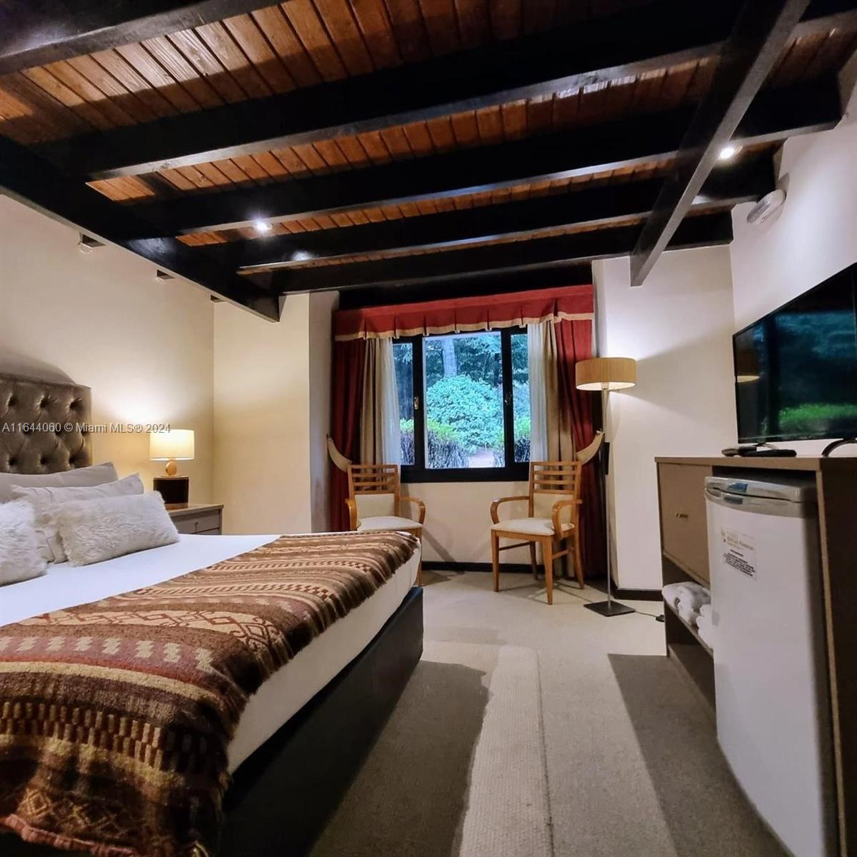 A bedroom features a bed with a patterned throw, exposed wood ceiling beams, and chairs — ARGENTINA Puerto Manzano Villa La Angostura, FL