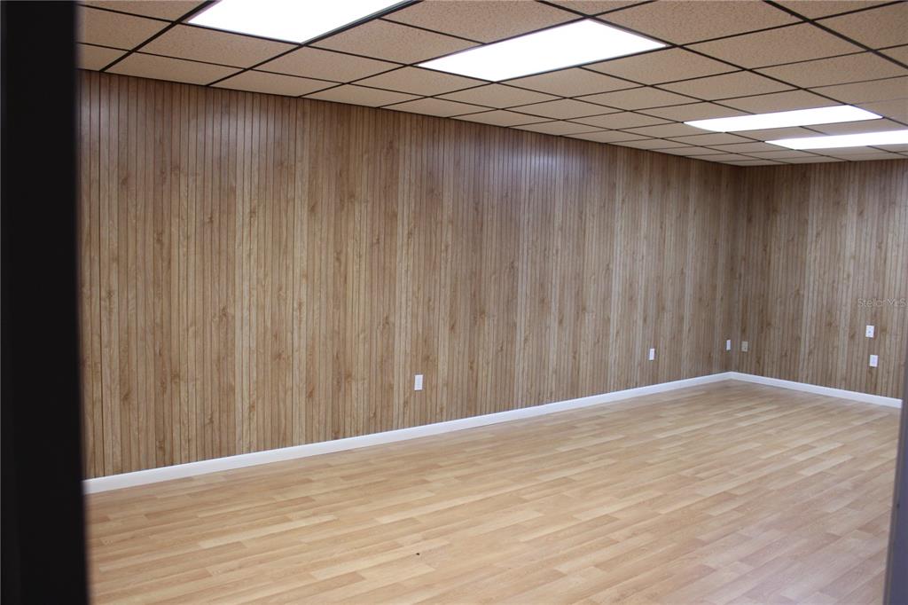 An empty room features wood-paneled walls, light wood-look flooring, and a drop ceiling with lights — 1224 66TH STREET N UNIT 1234,1238,1240, ST PETERSBURG, FL
