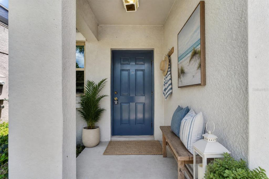 A blue front door is centered on a covered porch with a bench and decor — 10210 BOGGY MOSS DRIVE, RIVERVIEW, FL