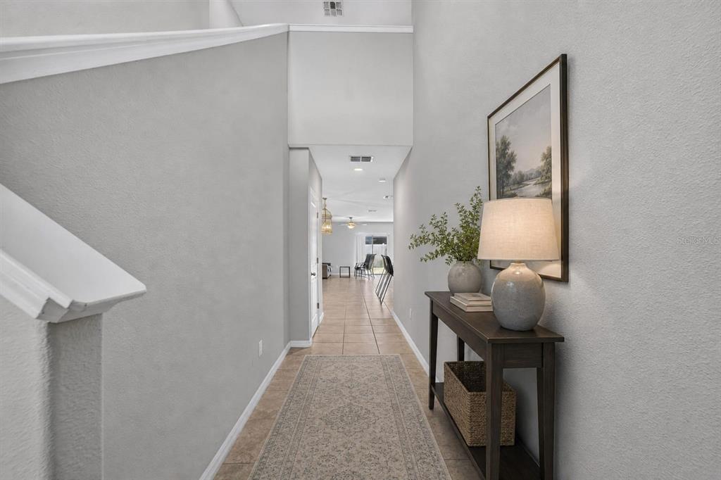 A hallway with tile flooring leads from a staircase toward an open living area — 10210 BOGGY MOSS DRIVE, RIVERVIEW, FL