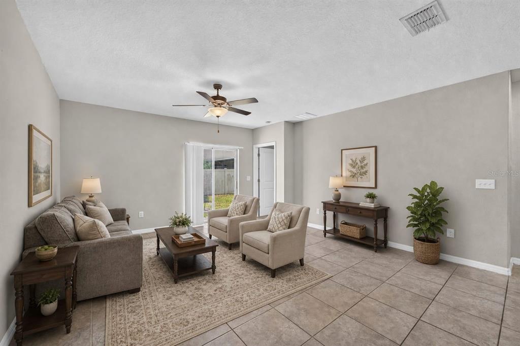 A living room features tile flooring, a ceiling fan, neutral walls, and sliding glass doors — 10210 BOGGY MOSS DRIVE, RIVERVIEW, FL
