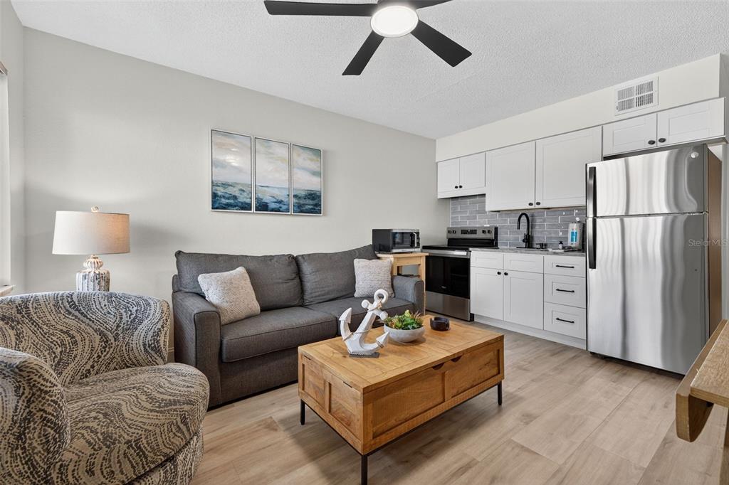 A small living room features a gray sofa, a wooden coffee table, and a kitchenette — 14251 GULF BOULEVARD UNIT 5, MADEIRA BEACH, FL