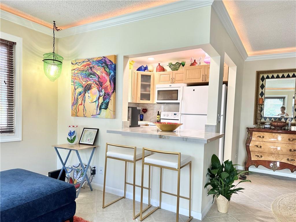 A kitchen with a breakfast bar, two gold-framed stools, and colorful wall art — 285 Oakridge Q # 285, Deerfield Beach FL 33442, DEERFIELD BEACH, FL