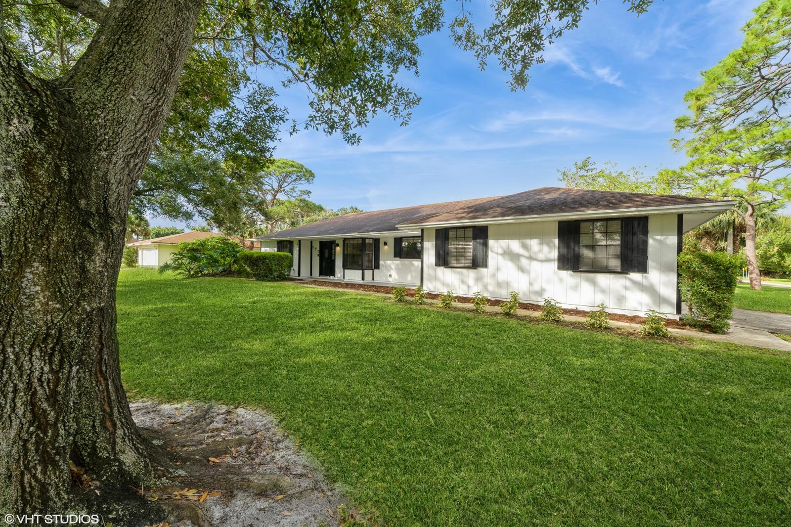 A white, single-story house with black shutters sits on a lawn with large trees — 595 11th Avenue, Vero Beach FL 32962, VERO BEACH, FL