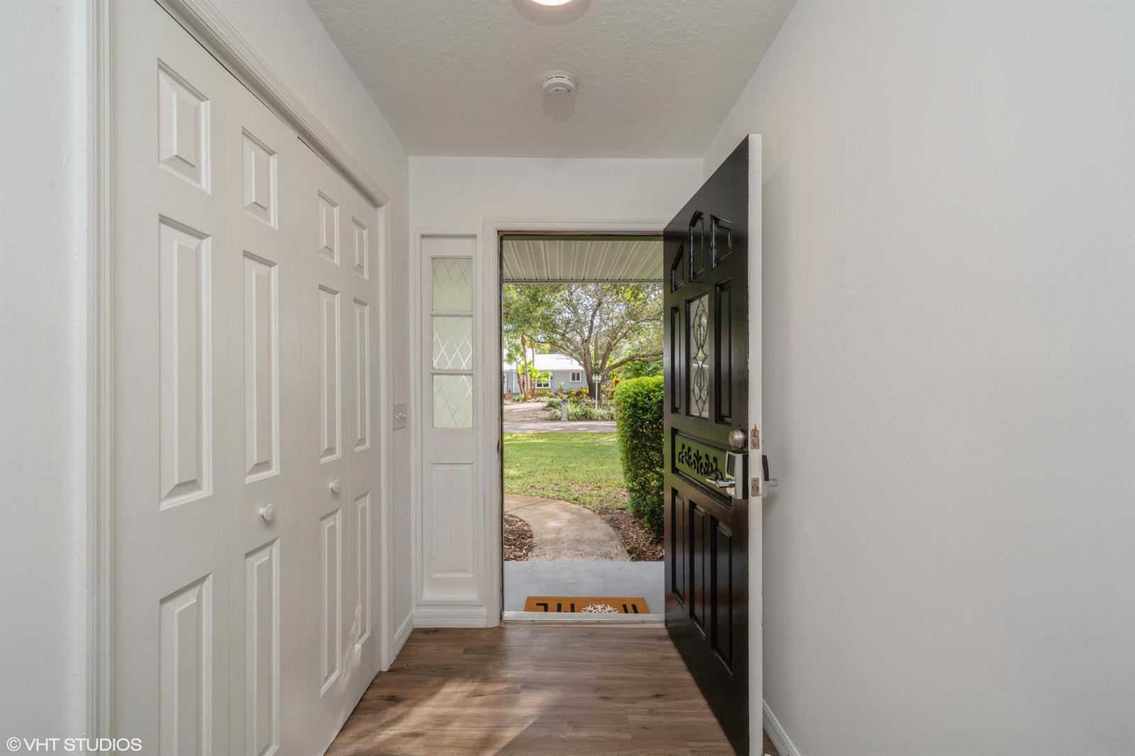 An entryway features wood-look flooring, a white closet, and an open black front door — 595 11th Avenue, Vero Beach FL 32962, VERO BEACH, FL
