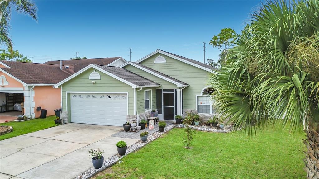 A green single-story house with a two-car garage, a front porch, and a palm tree — 7732 WATER OAK CT, KISSIMMEE, FL