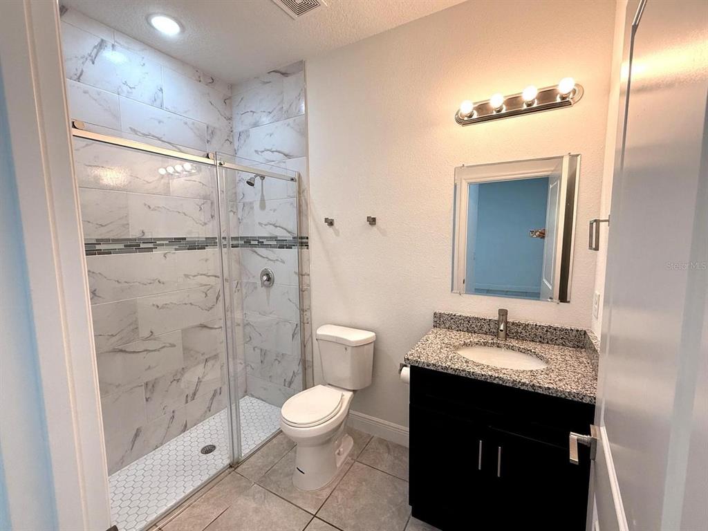 A bathroom features a glass-enclosed marble-tiled shower, a white toilet, and a dark vanity — 9130 N MENDOZA WAY, CITRUS SPRINGS, FL