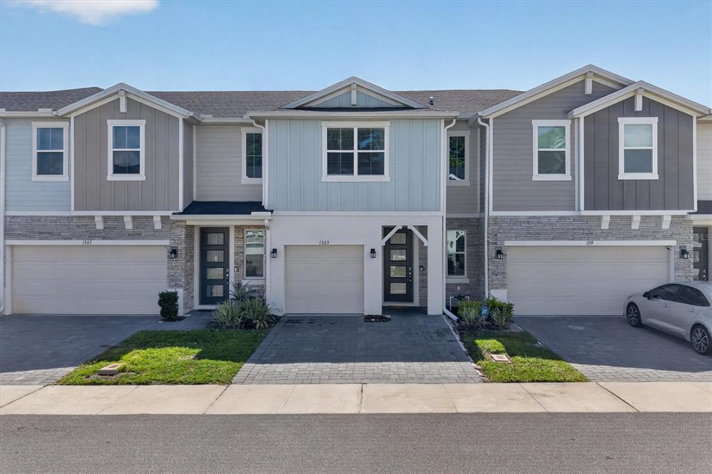 A three-unit townhouse complex with stone veneer, light blue siding, and paved driveways — 1363 CAPTIVA COVE, SANFORD, FL