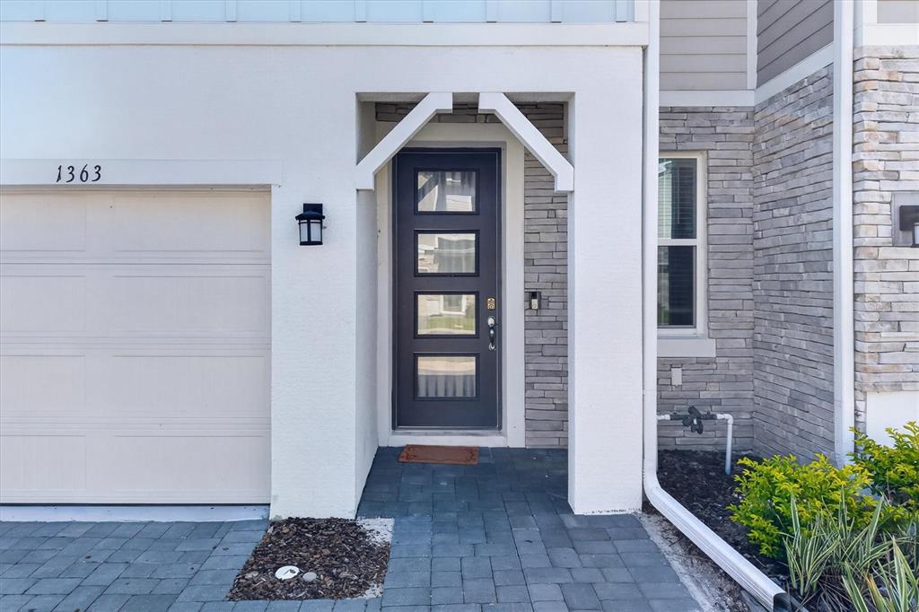A modern front entrance features a dark door with glass panels, stone siding, and pavers — 1363 CAPTIVA COVE, SANFORD, FL