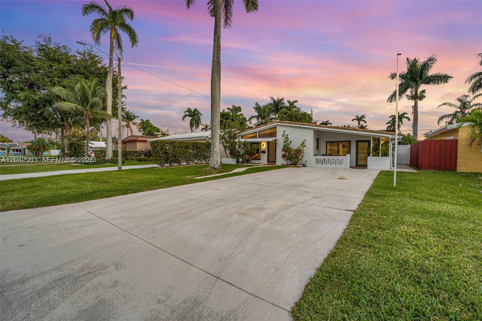 A single-story white house with a concrete driveway and palm trees under a sunset sky — 1514 Liberty St, Hollywood FL 33020, HOLLYWOOD, FL