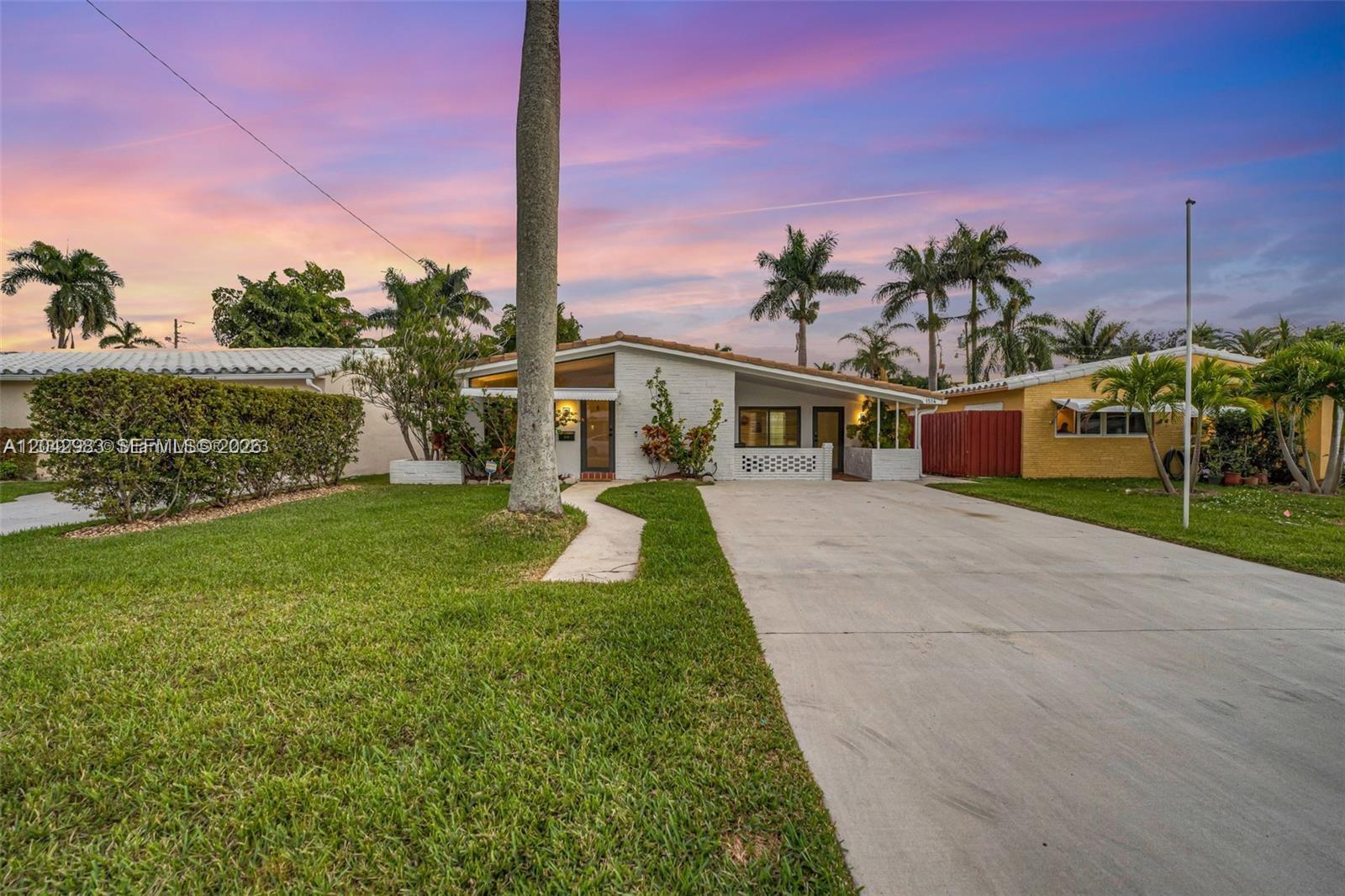 A single-story house with a white brick facade, concrete driveway, and palm trees at sunset — 1514 Liberty St, Hollywood FL 33020, HOLLYWOOD, FL