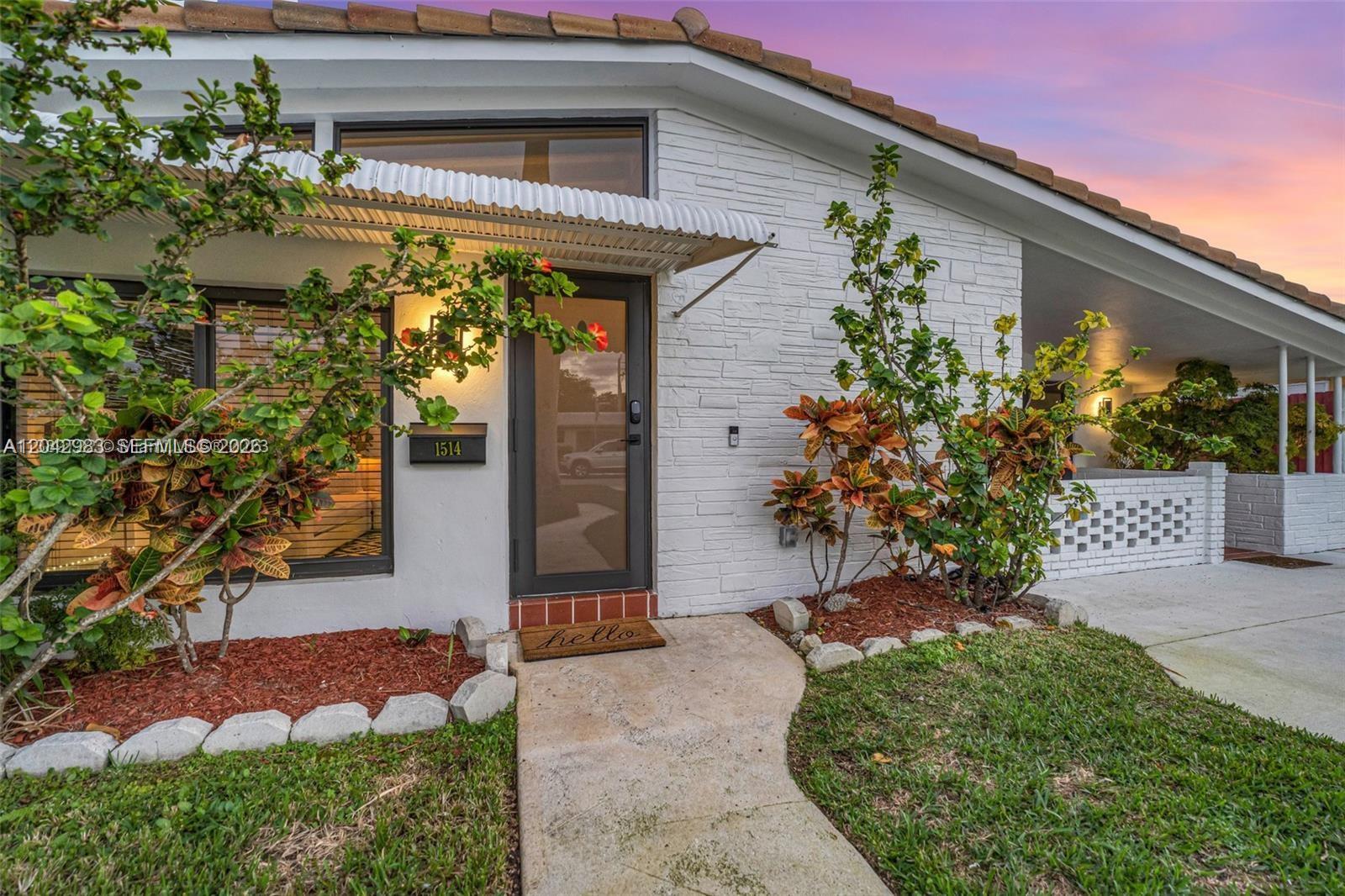 A white brick house exterior features a glass front door, metal awning, and landscaped yard — 1514 Liberty St, Hollywood FL 33020, HOLLYWOOD, FL