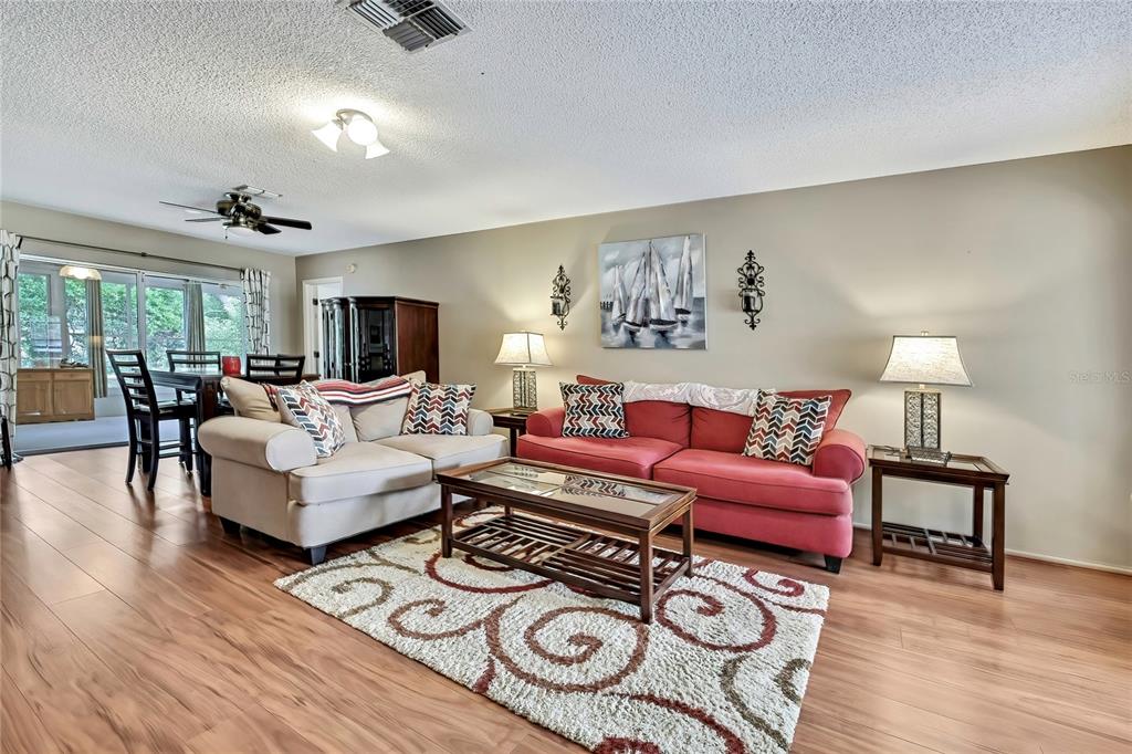 A living room features wood-look flooring, a red sofa, a beige loveseat, and a rug — 6517 OCEAN PINES LANE, SPRING HILL, FL