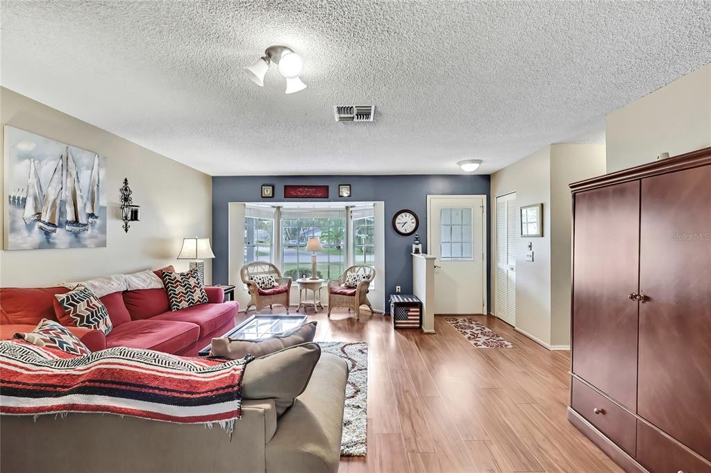 A living room features wood-look flooring, a red sofa, and a bay window with chairs — 6517 OCEAN PINES LANE, SPRING HILL, FL