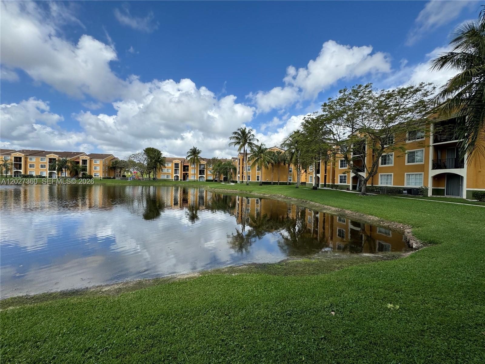 A pond reflects yellow apartment buildings surrounded by palm trees under a blue sky — 2200 E Preserve Way # 308, Miramar FL 33025, MIRAMAR, FL