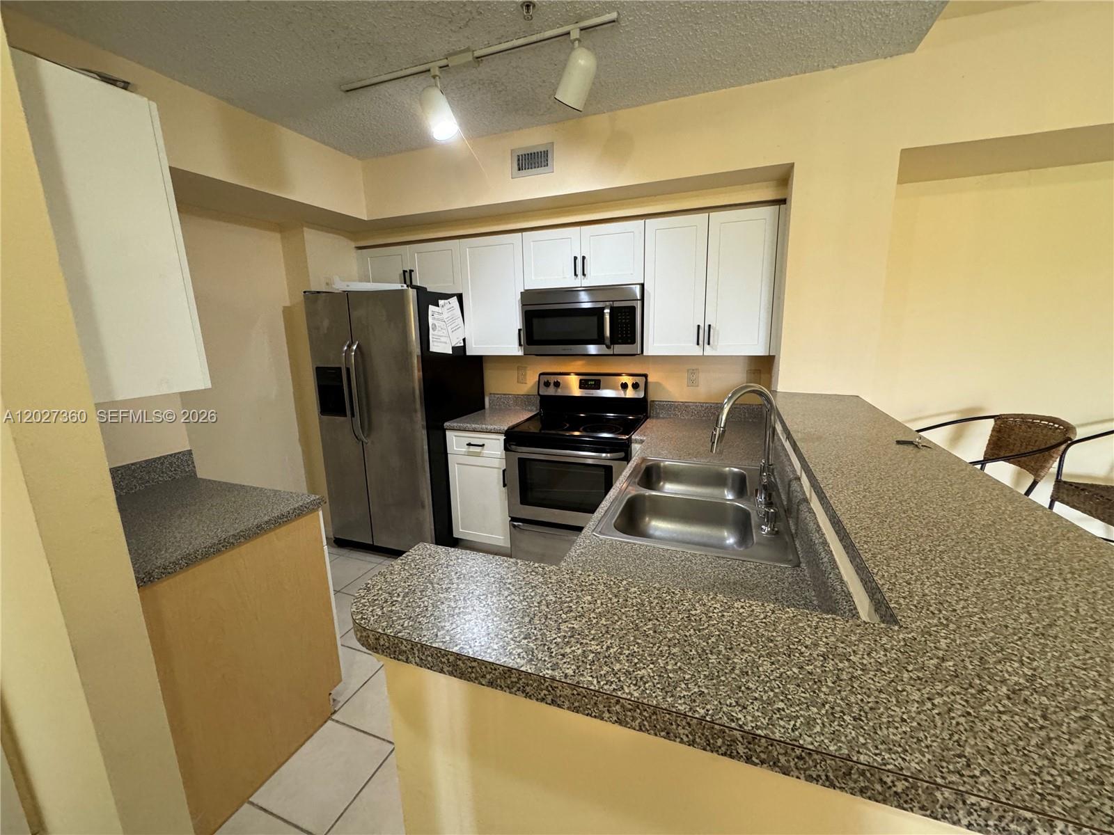 A kitchen features white cabinets, stainless steel appliances, and gray speckled laminate countertops — 2200 E Preserve Way # 308, Miramar FL 33025, MIRAMAR, FL