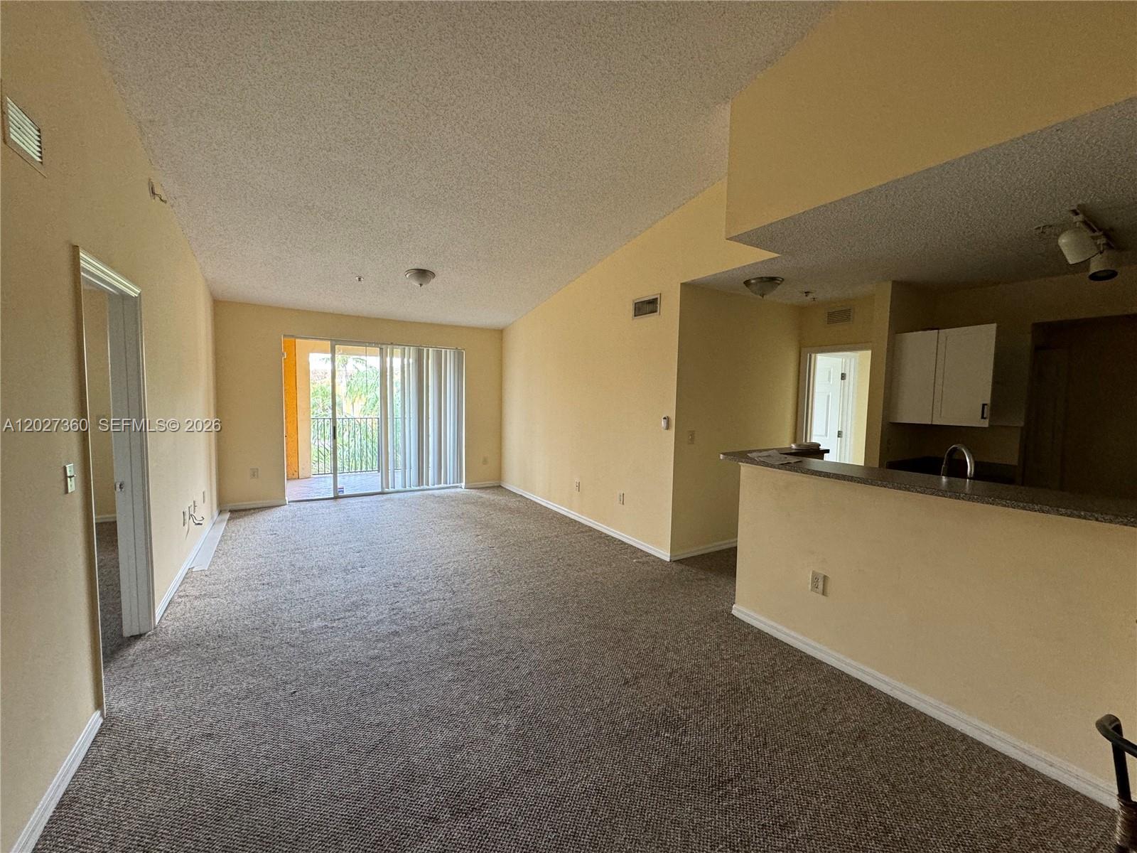 An empty living room with beige carpet, yellow walls, and a sliding glass door — 2200 E Preserve Way # 308, Miramar FL 33025, MIRAMAR, FL