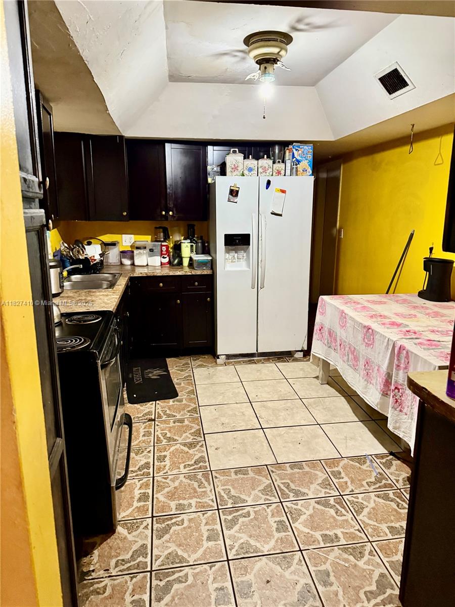 This kitchen features dark wood cabinets, a white refrigerator, and brown patterned tile flooring — 1180 NW 46th Ave, Lauderhill FL 33313, LAUDERHILL, FL