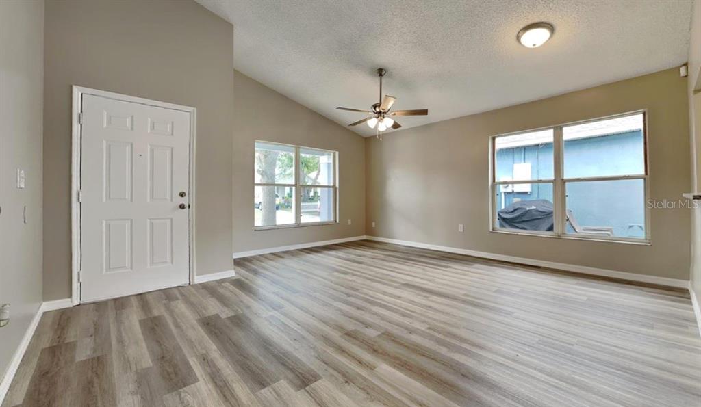 An empty living room features light-colored wood-look flooring, a ceiling fan, and two windows — 1226 FREMONT PARK AVENUE, ORLANDO, FL