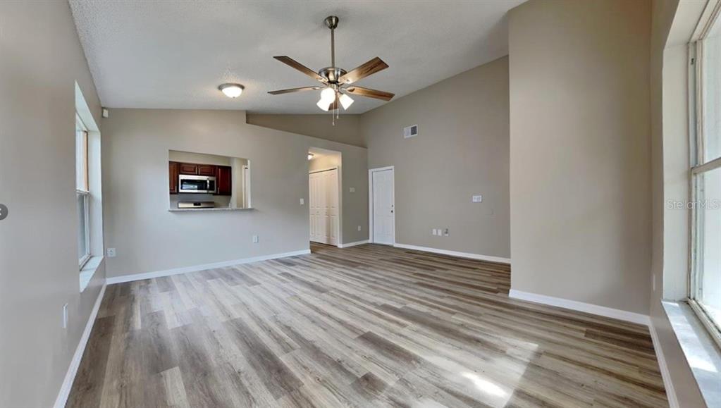 An empty living room features light-colored walls, wood-look flooring, a ceiling fan, and a pass-through window — 1226 FREMONT PARK AVENUE, ORLANDO, FL