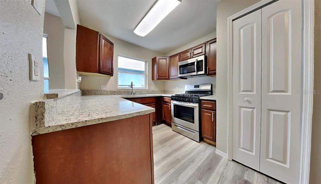 A kitchen features wood cabinets, granite countertops, stainless steel appliances, and light wood-look flooring — 1226 FREMONT PARK AVENUE, ORLANDO, FL