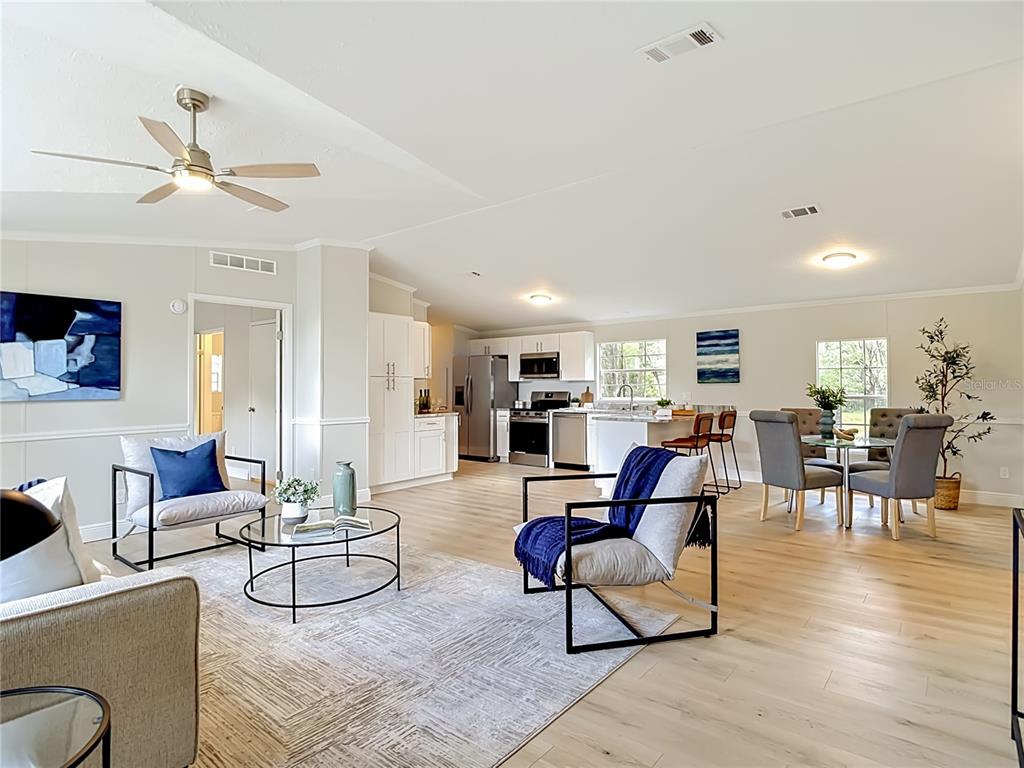 An open-concept living room and kitchen feature light wood flooring, white cabinetry, and modern furniture — 18118 PORSCHE PLACE, SPRING HILL, FL