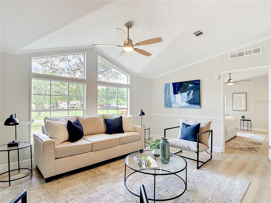 A living room features a beige sofa, glass coffee table, and vaulted ceilings with windows — 18118 PORSCHE PLACE, SPRING HILL, FL