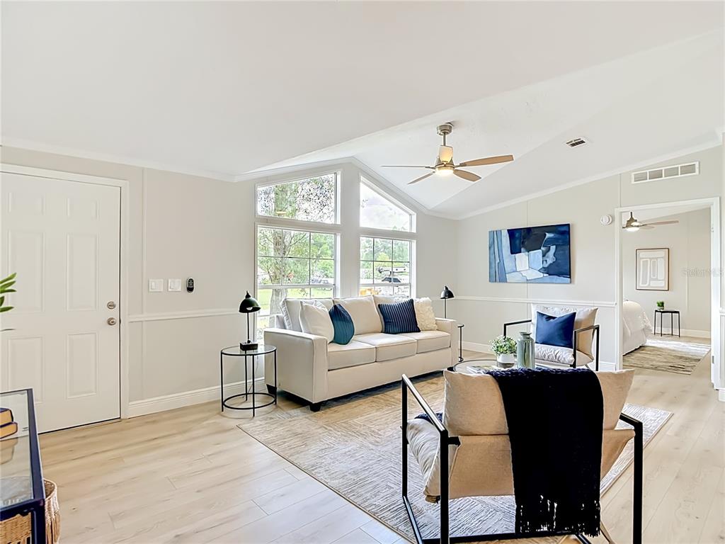 A bright living room features a white sofa, two armchairs, and large windows — 18118 PORSCHE PLACE, SPRING HILL, FL