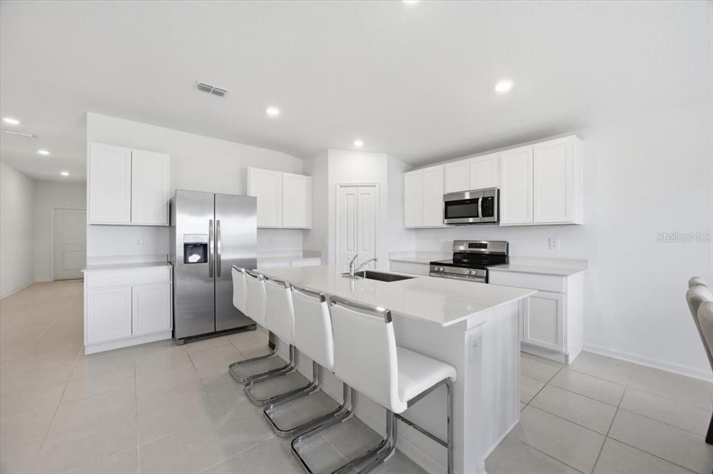 A modern kitchen features white cabinets, stainless steel appliances, and a central island with seating — 2350 MCKINLEY DRIVE, LAKE WALES, FL