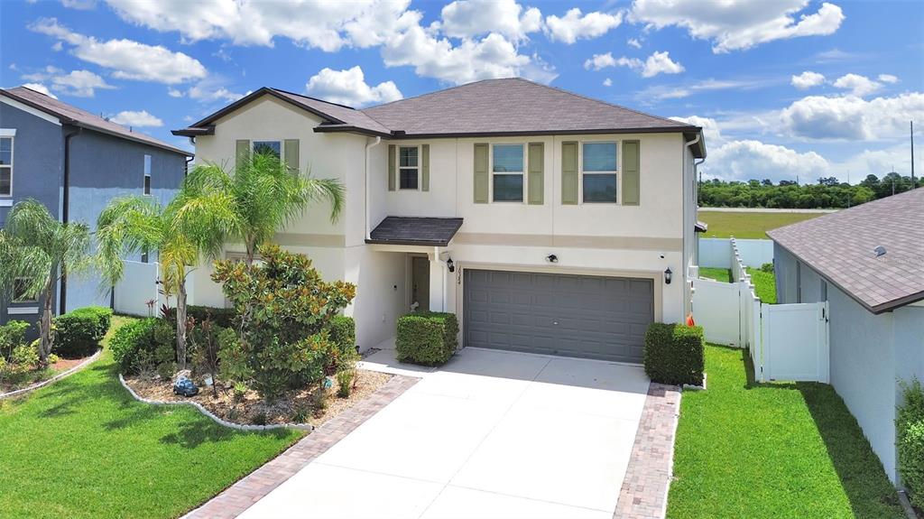 A two-story suburban house features a beige stucco exterior, a gray garage, and landscaping — 10384 SCARLET SKIMMER, RIVERVIEW, FL