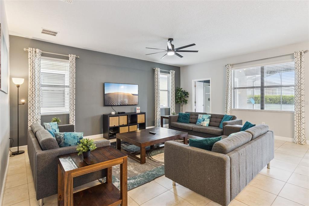 A living room features gray sofas, a dark wood coffee table, and a wall-mounted television — 9027 SHADOW MOUNTAIN STREET, DAVENPORT, FL