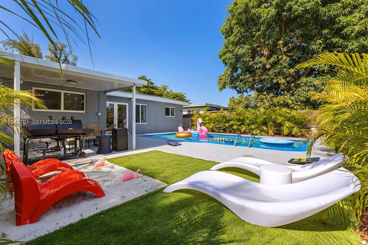 A backyard features a swimming pool, a covered patio, lounge chairs, and artificial turf — 1240 NE 159th St, North Miami Beach FL 33162, NORTH MIAMI BEACH, FL