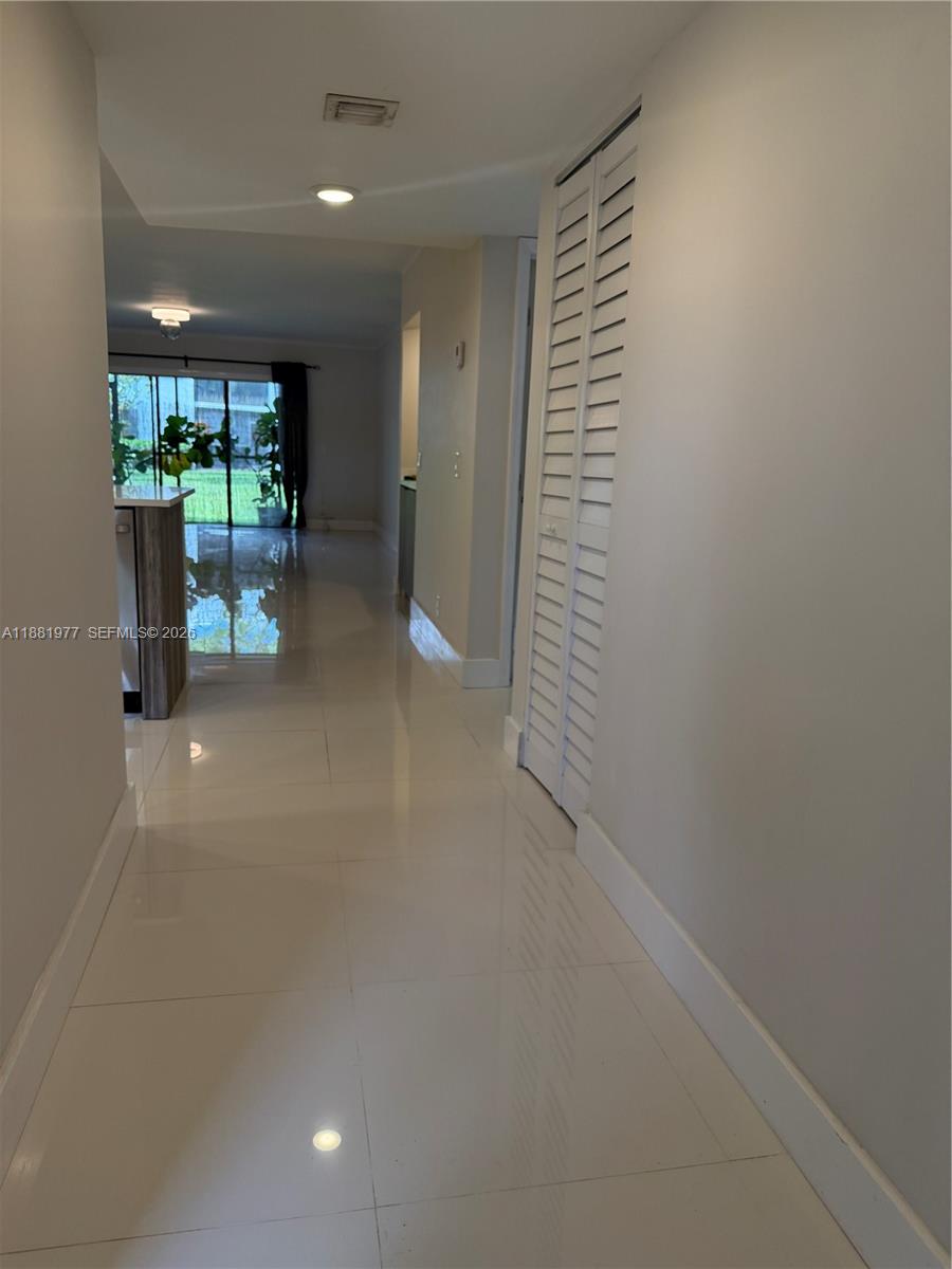 A hallway with white tile floors leads toward a kitchen and a glass sliding door — 16531 Blatt Blvd # 103, Weston FL 33326, WESTON, FL