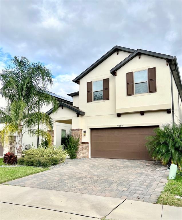 A two-story house with a beige stucco exterior, brown shutters, and a paved driveway — 9359 JUNIPER MOSS CIRCLE, ORLANDO, FL