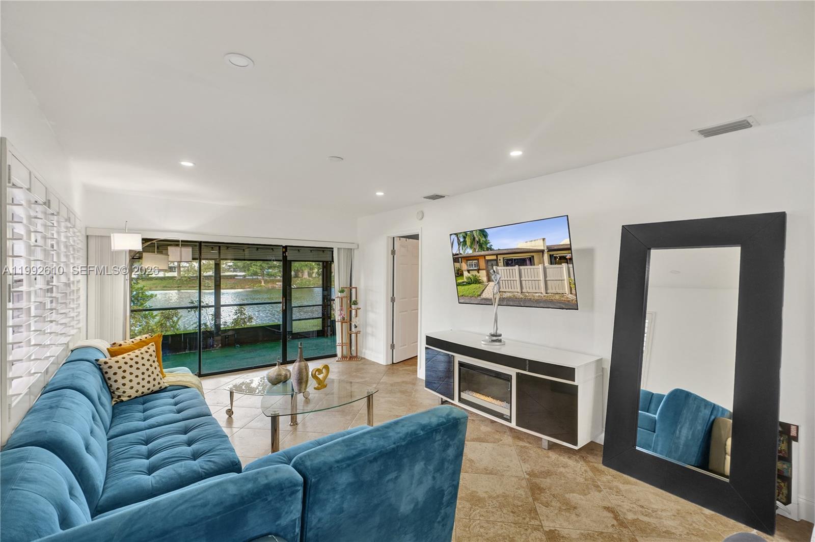 A living room features a blue sectional sofa, a glass coffee table, and a television — 707 Banks Rd, Margate FL 33063, MARGATE, FL