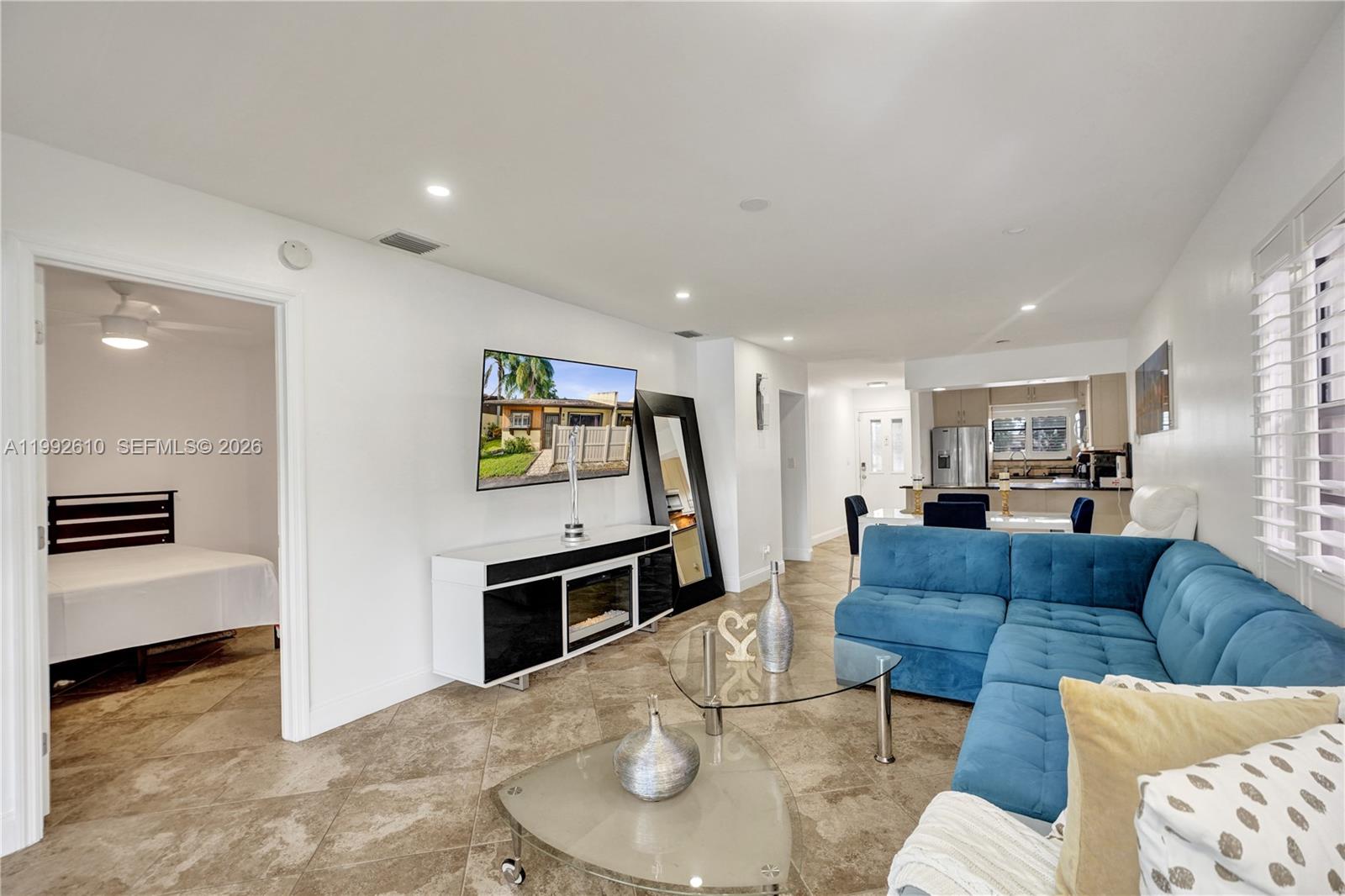 A living room features a blue sectional sofa, tile flooring, and a wall-mounted television — 707 Banks Rd, Margate FL 33063, MARGATE, FL