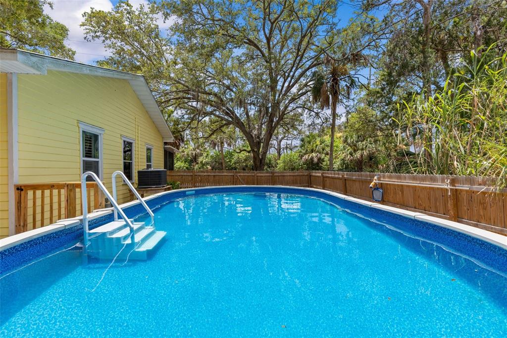 An above-ground swimming pool sits in a backyard next to a yellow house with siding — 190 OSOWAW BOULEVARD, SPRING HILL, FL