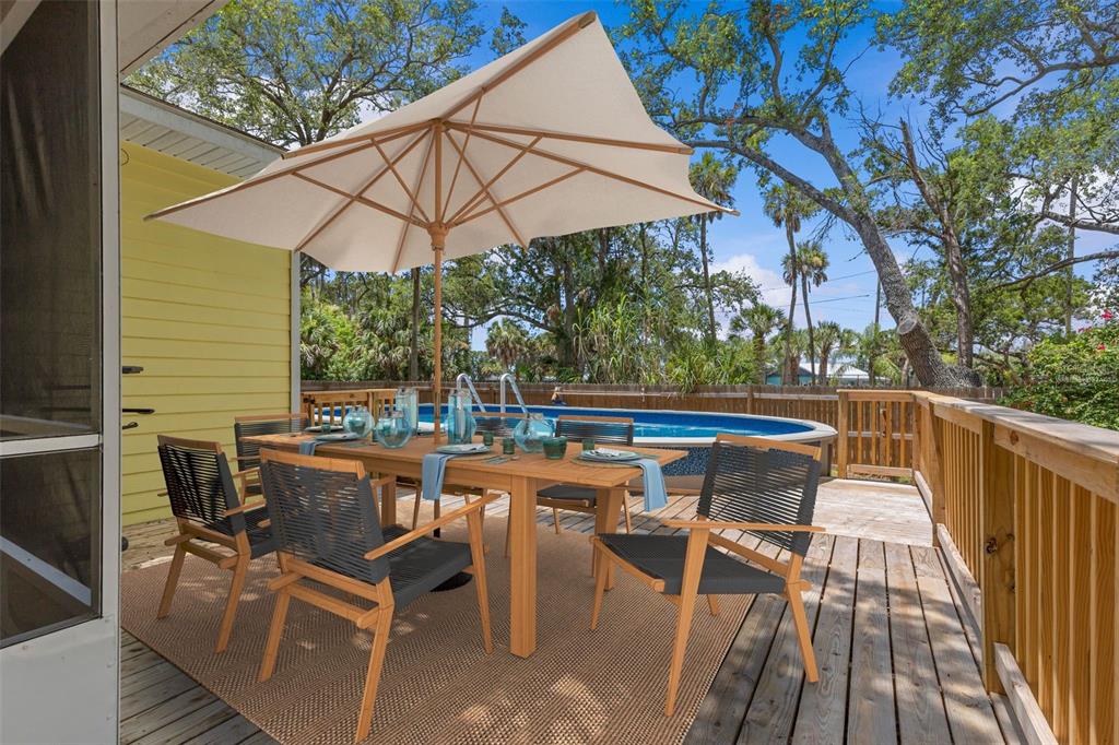 A wooden deck features a dining set with an umbrella overlooking an above-ground pool — 190 OSOWAW BOULEVARD, SPRING HILL, FL