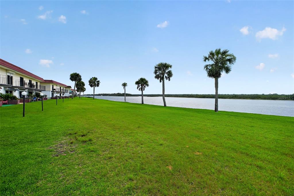 A grassy lawn stretches toward a river lined with palm trees next to a building — 24 S OCEAN PALM DRIVE UNIT 24, FLAGLER BEACH, FL